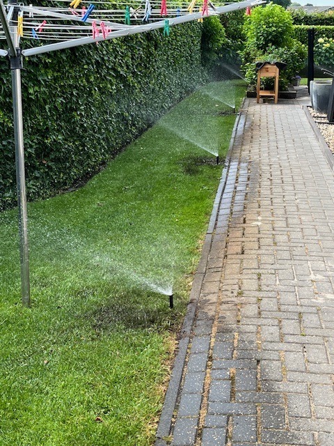Twee sproeiers op gazon langs tuinpad
