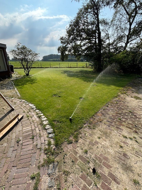 Sproeier op gazon met historische muur op de achtergrond